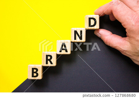 Brand symbol. Concept word Brand on beautiful wooden blocks. Beautiful yellow and black background. Businessman hand. Business brand concept. Copy space. 127868680