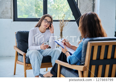 Serious teen girl in session in office of professional psychologist, therapist 127869799