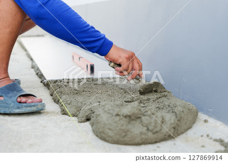 Close-up of a worker smoothing gray mortar with a tool, ensuring the surface is ready for precise tile placement. Close-up of a worker smoothing gray mortar with a tool, ensuring the surface is ready for precise tile placement. 127869914