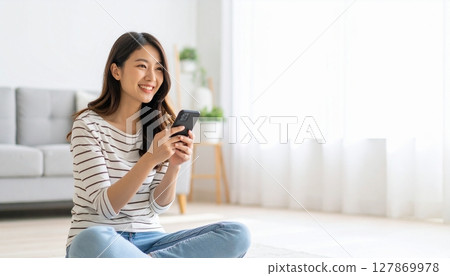 一位微笑的日本女士在客廳操作智慧型手機 一位微笑的日本女士在客廳操作智慧型手機 127869978