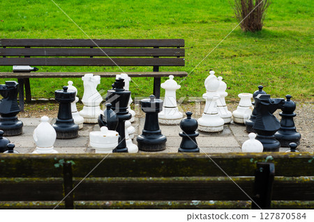 A vibrant park setting with oversized chess pieces inviting strategic play among leisurely gathering spots and lush greenery A vibrant park setting with oversized chess pieces inviting strategic play among leisurely gathering spots and lush greenery 127870584