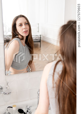 A beautiful young woman with braces looks in the mirror and smiles at her reflection. 127870603