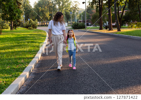 Mother and daughter walking on park pathway in casual outfits 127871422