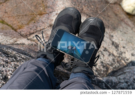 Close-up of hikers legs on rocky ground with smartphone placed on shoes reflecting a selfie 127871559