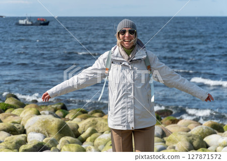 Woman in a white jacket with arms outstretched smiles widely while standing on the round moss-covered boulders n Teriberka Woman in a white jacket with arms outstretched smiles widely while standing on the round moss-covered boulders n Teriberka 127871572