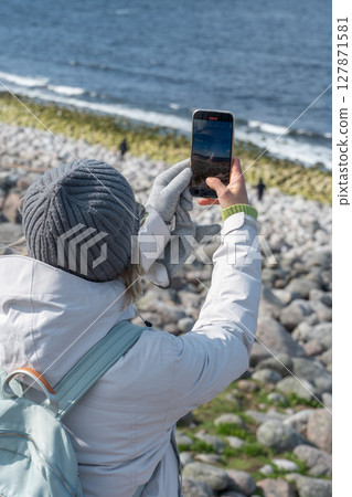 Woman in winter clothes taking a selfie on a rocky Arctic coast in a protected reserve in Teriberka 127871581