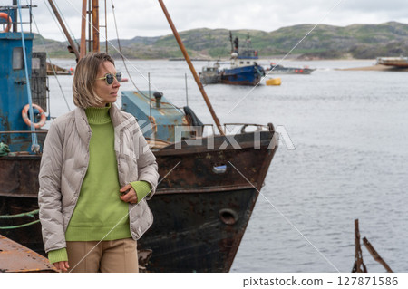 Woman standing near rusty abandoned fishing boats at the ship graveyard in Teriberka 127871586