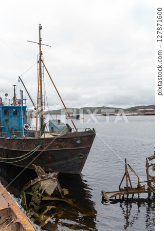 Rusty fishing boats and sunken shipwrecks in the famous ship graveyard of Teriberka under overcast skies 127871600