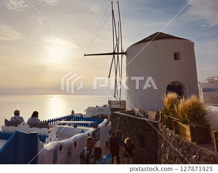 Restaurant visitors with a windmill on Santorini are waiting for a beautiful sunset 127871925