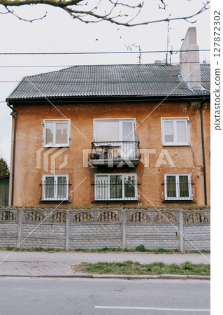old brown building with a balcony. The building is surrounded by a fence.  127872302