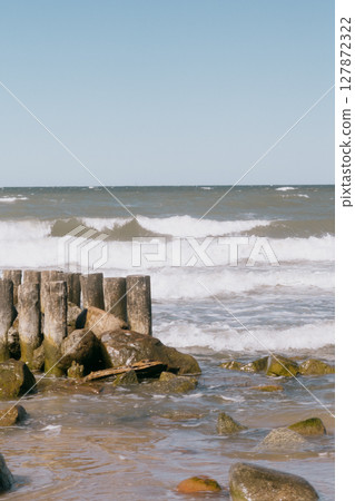 rocky beach with a wooden pier and a pond. The sky is clear and blue.  127872322