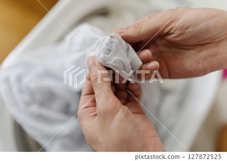 Top view of male hands examining white clothing, checking fabric surface for potential staining before soaking in washing basin, close-up. Concept of domestic work, housekeeping and household. Top view of male hands examining white clothing, checking fabric surface for potential staining before soaking in washing basin, close-up. Concept of domestic work, housekeeping and household. 127872525