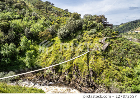 Suspension pedestrian bridge of the Barca da Amieira walkways in Amieira do Tejo, Portugal. Suspension pedestrian bridge of the Barca da Amieira walkways in Amieira do Tejo, Portugal. 127872557