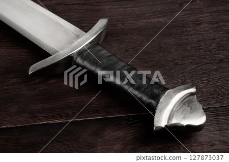 Medieval sword on wooden background. 127873037