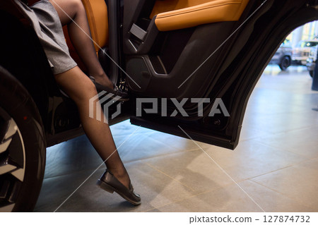 A fashionable woman wearing high heels elegantly stepping out of a black car in the city at night 127874732