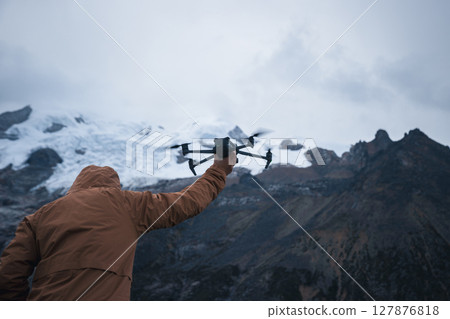 Photographer taking photo of snow capped mountain with a drone on high altitude grassland mountain top 127876818