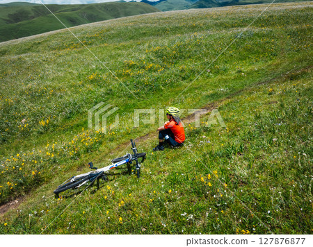 Aerial view of woman riding mountain bike on flowering grassland mountain 127876877