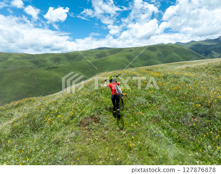 Woman carrying mountain bike on beautiful flowering grassland mountain top 127876878