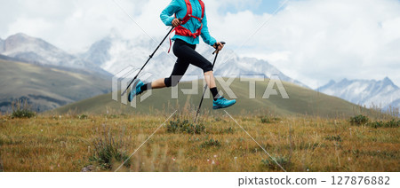 Fitness woman trail runner running in grassland with snow capped mountains in the background 127876882