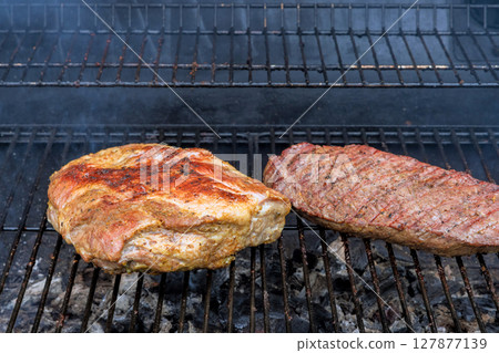 Juicy cuts of meat sizzle on grill, releasing mouthwatering aromas as they cook during an outdoor barbecue. Juicy cuts of meat sizzle on grill, releasing mouthwatering aromas as they cook during an outdoor barbecue. 127877139