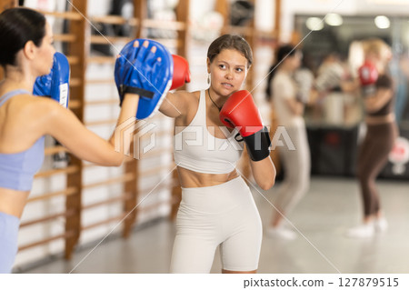 Woman works out strength and speed of boxing punch mitts with help of partner in boxing paws 127879515