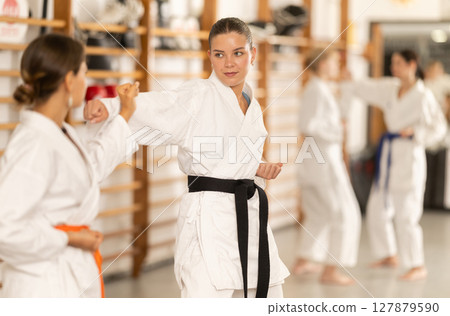 Young female attendee of karate classes fighting with partner in sports hall Young female attendee of karate classes fighting with partner in sports hall 127879590