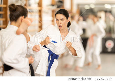 Young female attendee of karate classes fighting with partner in sports hall Young female attendee of karate classes fighting with partner in sports hall 127879742