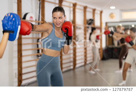 Woman works out strength and speed of boxing punch mitts with help of partner in boxing paws 127879787