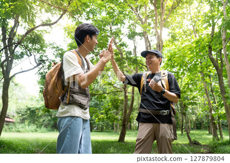 Father and Son Celebrating Together. Sharing a high-five in a vibrant outdoor setting. 127879804