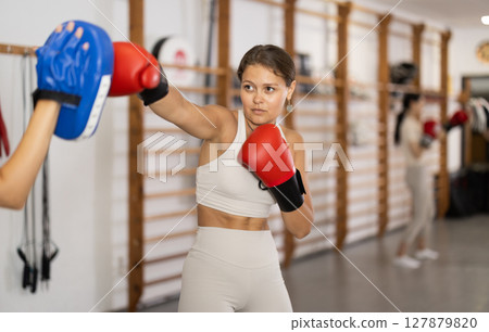 Young girl training boxing kicks on punch mitts Young girl training boxing kicks on punch mitts 127879820