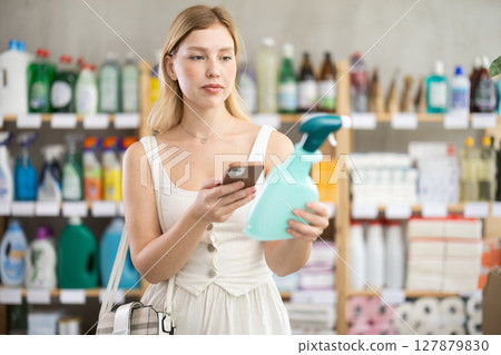 woman in summer clothes scans a qr code on a package of surface cleaning spray 127879830