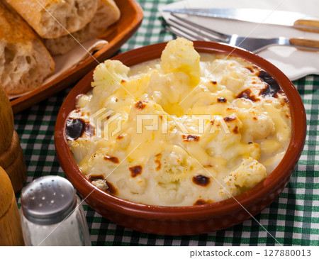 Tasty baked cauliflower with bechamel sauce in clay pot at table 127880013