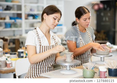 Two young women pottery workshop workers sculpt from raw clay 127880115