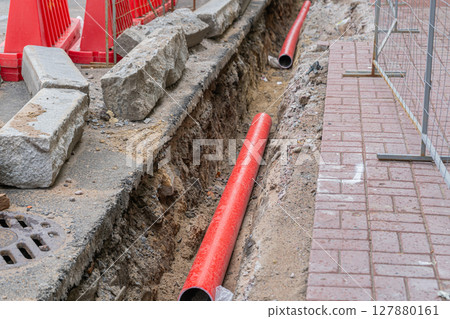 Road repairs, pipe, pile of sand. Red and white plastic barriers blocking the road. 127880161