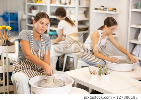Three young women sits near potter wheel and makes clay crafts 127880185