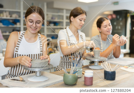 Three craftsperson are busy sculpting from clay and painting ceramic products 127880204