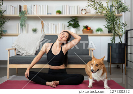 Relaxing Yoga Session with Pet. Woman practicing yoga alongside her corgi in a cozy living space. Relaxing Yoga Session with Pet. Woman practicing yoga alongside her corgi in a cozy living space. 127880222