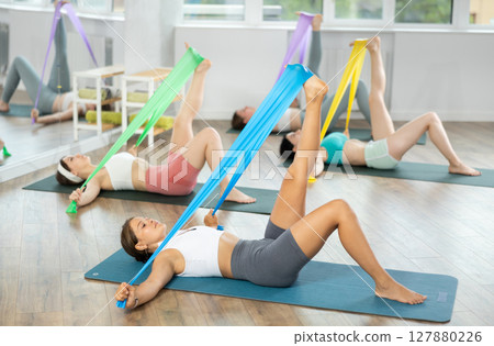 Group of women with working out with rubber bands lying on your back in gym Group of women with working out with rubber bands lying on your back in gym 127880226