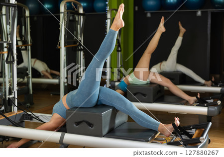 Woman in sports top and leggings doing exercises on reformer Woman in sports top and leggings doing exercises on reformer 127880267