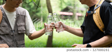 Father and Son Hydrating Together. Sharing water bottles during an outdoor adventure. 127880281