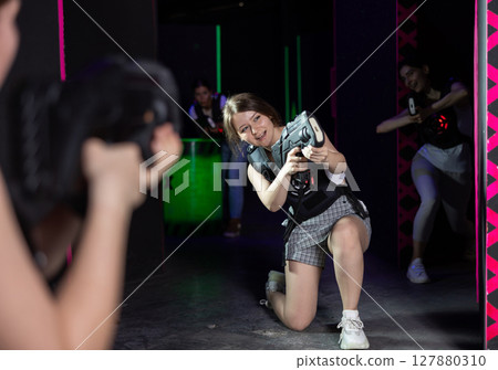 Joyous girl with laser pistol playing laser tag with girlfriends on labyrinth 127880310