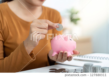 Savings and Financial Planning. Individual adding coins to pink piggy bank. 127880311