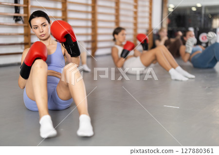 Girls in boxing gloves are sitting on floor, doing abdominal exercise and working with hands 127880361