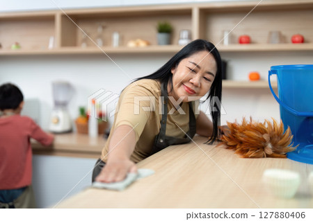 Home Cleaning and Family Time. A mother enjoying cleaning while her son plays a supportive role. 127880406