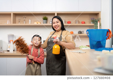 Family Cleaning Day. A mother and son posing with cleaning tools in a bright kitchen. 127880408