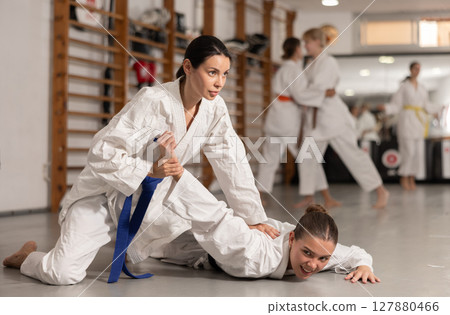 Positive young girl twisting her opponent's arm during judo classes 127880466