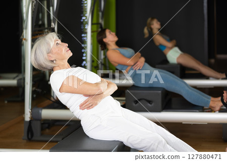 Woman sitting on reformer and bending over 127880471