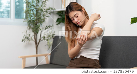 Elbow Pain and Discomfort. Young woman rubbing her elbow in pain at home. 127880479