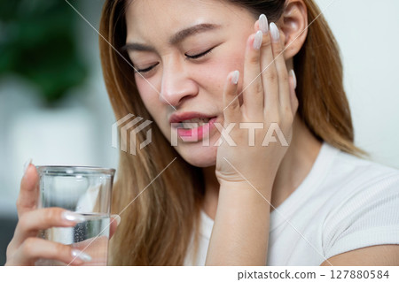 Dental Pain Relief. Woman holding face in discomfort while drinking water. 127880584