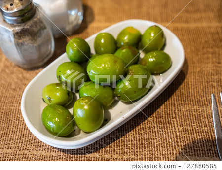White plate with delicious green olives with pits closeup 127880585